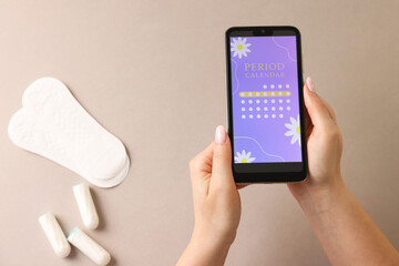 Menstruation. Woman holding smartphone with period calendar application on beige background, top view