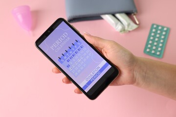 Menstruation. Woman holding smartphone with period calendar application on pink background, above view