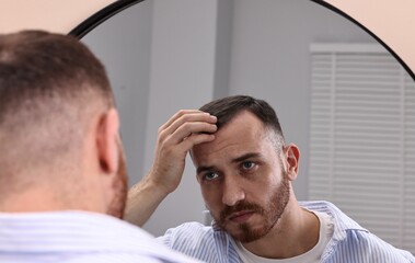 Fototapeta premium Baldness problem. Man with receding hairline near mirror in bathroom