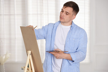 Fototapeta premium Young man painting picture on easel in artist's studio