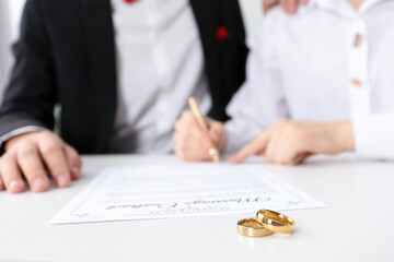 Newlyweds signing marriage contract and wedding rings on desk, selective focus