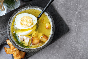 A bowl of homemade chicken broth with eggs and crusty bread served on a rustic wooden board