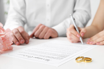Newlyweds signing marriage contract and wedding rings on desk, selective focus