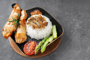 Grilled chicken kebabs with rice, fried mushrooms and vegetables, served on a black plate in a cosy setting