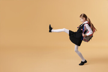 Schoolgirl with backpack on brown background. Space for text