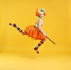 Girl dressed like clown jumping with hula hoop on yellow background. Surprise party