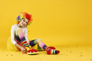 Cute girl dressed like clown and confetti on yellow background, space for text. Surprise party