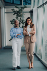 Obraz premium Two businesswomen smiling with arms crossed in modern office hallway