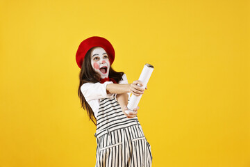 Happy girl dressed like mime with confetti popper on yellow background. Surprise party