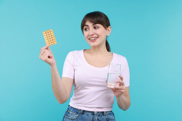 Smiling woman with contraceptive pills and glass of water on light blue background