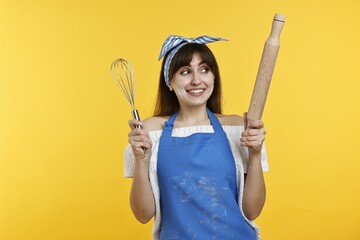 Woman with rolling pin and whisk on yellow background
