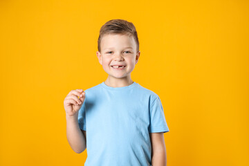 Cute little boy with missing tooth on orange background. Waiting for tooth fairy