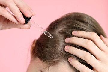 Hair loss problem. Girl applying serum onto hairline on pink background, closeup