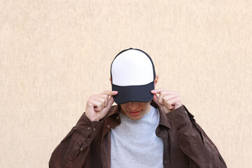 Man in stylish baseball cap near beige wall. Mockup for design