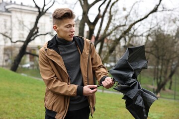 Man with broken umbrella fighting wind under rain outdoors