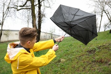 Man with broken umbrella fighting wind under rain outdoors