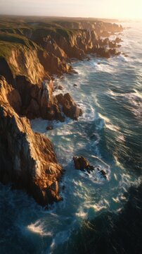 Steep coastal cliffs drop into foaming ocean waves along a rugged shoreline illuminated by warm sunset light.