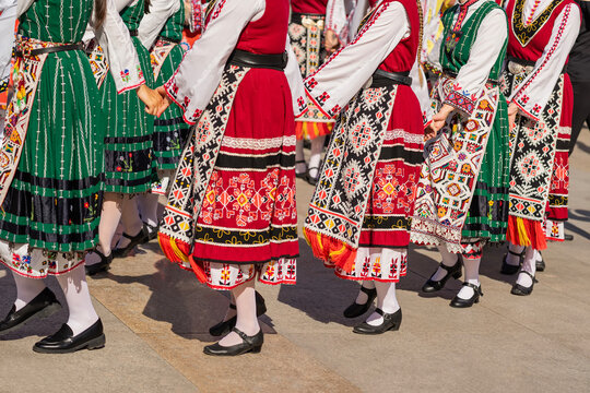 Women in traditional Balkan dresses perform group folk Bulgarian dance in sunlight. Traditional dance. Women in Bulgarian folk costumes dancing at outdoor festival