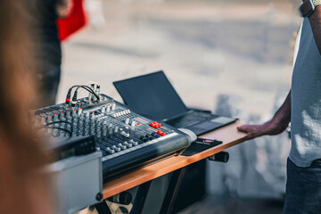 Professional audio mixing console with laptop set, outdoor event. Sound engineer adjusting settings...