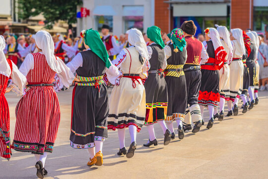 Group of people in folk costumes dancing in traditional circle at cultural event. Variety of embroidered dresses represents different regional styles and traditions