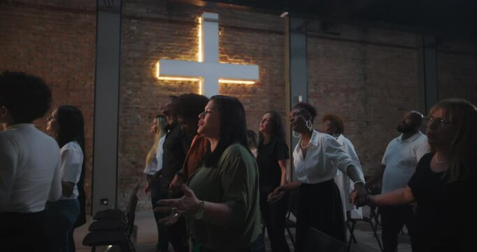 People holding hands in church, praising with joyful expressions, illuminated cross shining in background, spiritual moment, group of diverse individuals worshiping