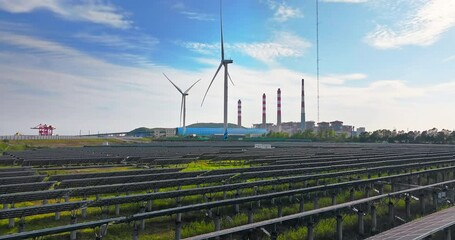 Aerial view of energy landscape with solar panel arrays wind turbines and a fossil fuel power plant under blue sky.