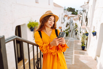 Beautiful tourist in hat and backpack with texting or blogging with phone in hands outdoors. Young...