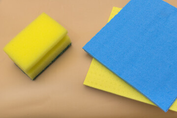 Close-up of sponges for cleaning, in blue and yellow colors on a beige background. A simple home-cleaning product