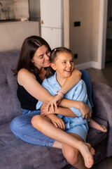 Obraz premium Mom and daughter are sitting at home on the couch, hugging