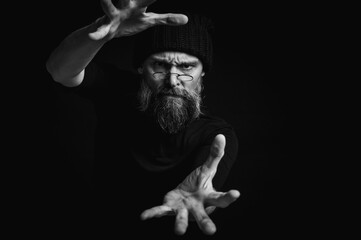 Black and white, dramatic portrait of an energetic man with a beard and glasses, reaching towards...