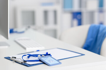 Clipboard with paperwork and badge on desk in doctor's office, closeup. Space for text
