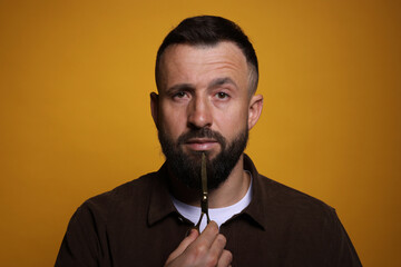 Bearded man with scissors on orange background