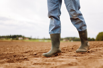 A farmer in rubber boots in an agricultural field on a cloudy day. Close-up of a woman in boots...