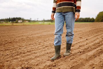 A farmer in rubber boots in an agricultural field on a cloudy day. Close-up of a woman in boots...