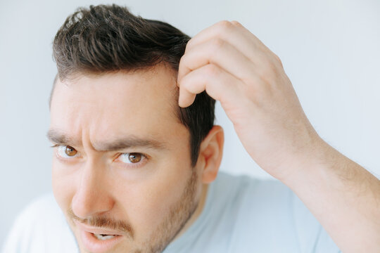 Man examines his hairline in a bright, minimalistic room