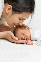 Mother kissing Newborn Baby. Happy Mum embracing sleeping Baby. Little New born Child sleep on white Blanket. Childbirth and Childcare. Mother's day holiday. Mother Love Baby