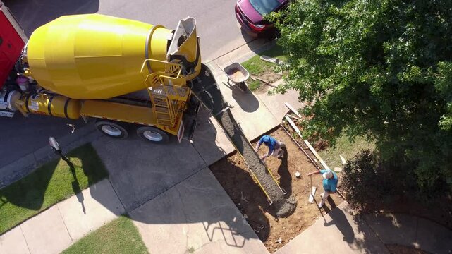 Overhead view of laborers using a cement mixer to pour wet cement into a driveway.