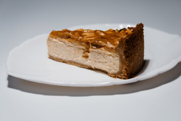 Slice of delicious caramel cheesecake with peanut topping on a white plate against a plain background, close-up view