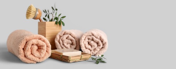 Rolled towels, green twigs, brush and soap bar on grey background with space for text