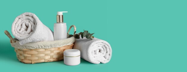 Wicker basket with clean soft towels, shampoo and cream on turquoise background with space for text