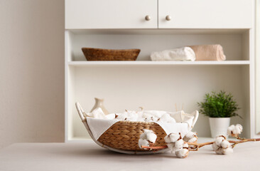 Basket with cotton flowers with sprig on white table in room