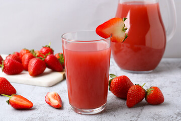 Glass and jug of tasty strawberry juice on grey table