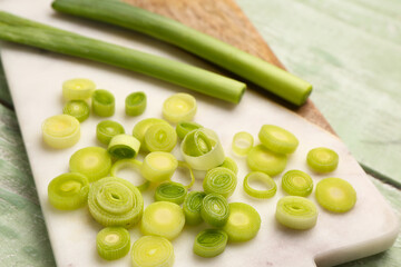 Board with slices of fresh leek on green wooden background