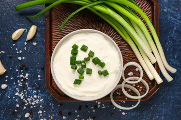Bowl of tasty sour cream with scallion and onion on blue background