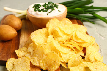 Bowl of tasty sour cream with sliced green onion and potato chips on grey background
