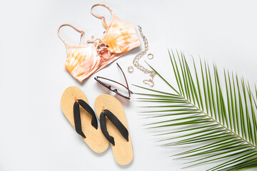 Stylish bikini top, flip-flops, sunglasses, accessories and palm leaf on light background