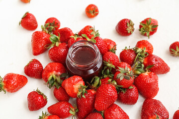 Jar of sweet strawberry jam and fresh berries on light background