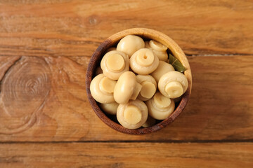 Bowl with canned mushrooms on wooden background