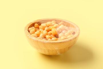 Bowl of fresh chickpeas covered with plastic food wrap on yellow background