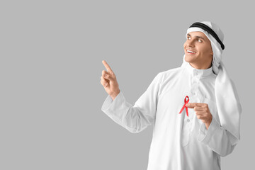 Handsome Muslim man with red ribbon pointing at something on grey background. AID awareness concept